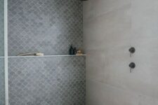 a concrete bathroom with an accent fish scale tile wall and dark brass fixtures is a pretty and cool space