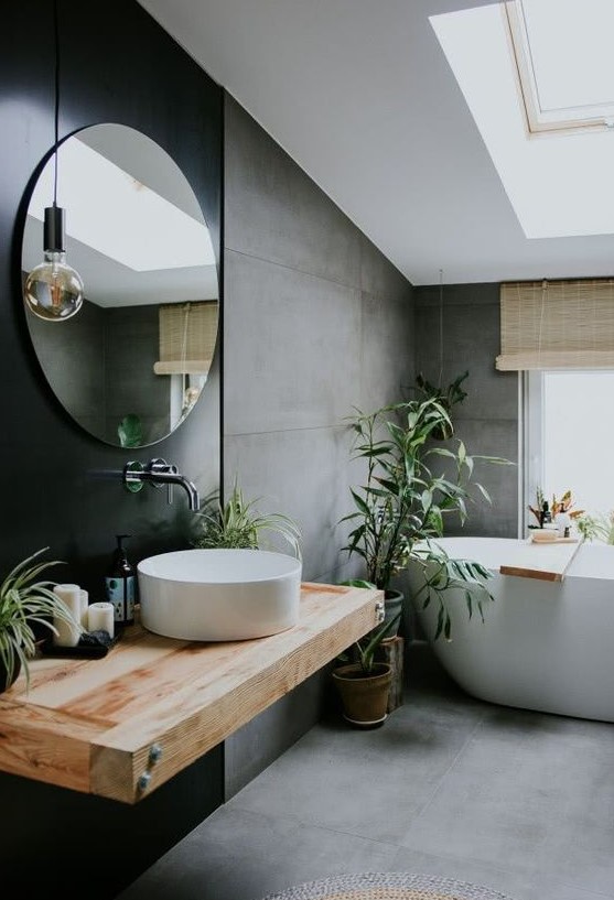 a contemporary attic bathroom with concrete walls and a floor, a black accent wall with a floating vanity and a round mirror