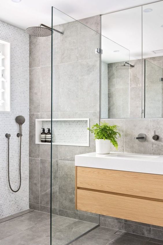 a contemporary grey bathroom clad with large scale tiles and penny ones, with a floating wooden vanity and a large window