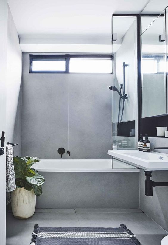 a contemporary grey bathroom clad with large scale tiles, with a small window and black fixtures to make it look bolder