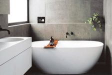 a contemporary grey bathroom clad with tiles, with a floating vanity and an oval tub plus greenery to refresh the space
