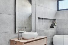 a contemporary grey bathroom with large scale tiles, an oval tub and a shower space, a stained vanity, an arched mirror