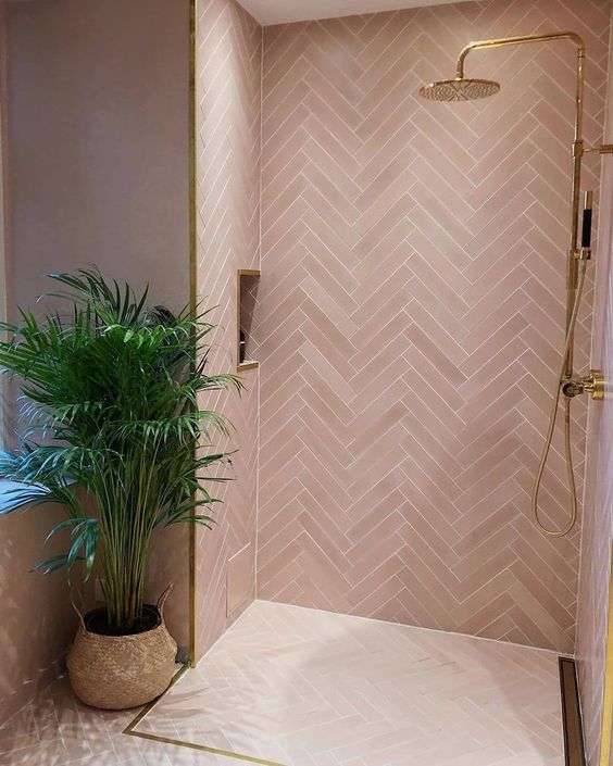 a contemporary pink bathroom clad with pink tiles in a herringbone pattern, gold fixtures and frames for a glam look