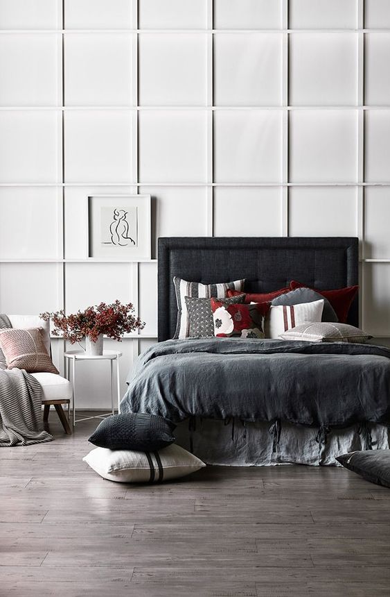 A contrasting bedroom with a white paneled wall, a blakc upholstered bed, dark bedding and a white chair looks ultra modern