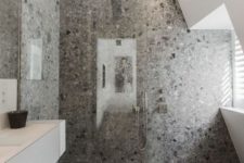 a cool minimalist grey bathroom with grey terrazzo in the shower, a white vanity and windows for natural light
