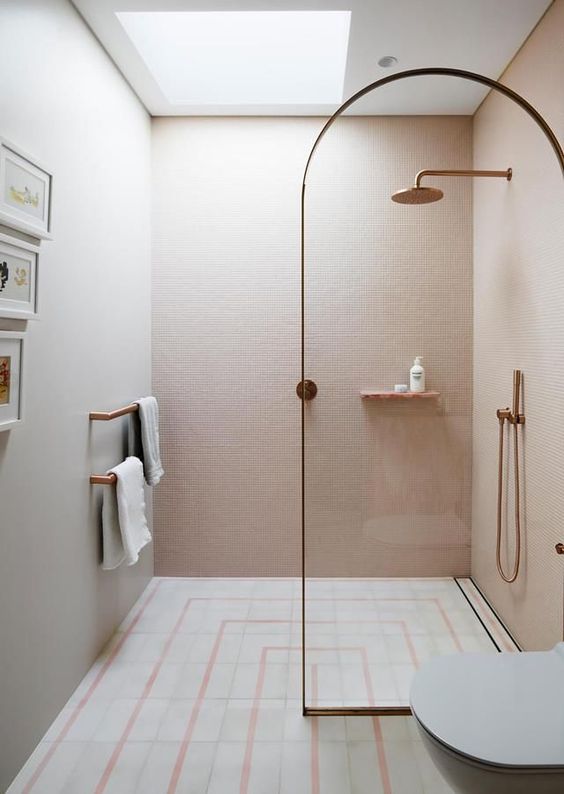 a cute contemporary bathroom with blush tiles on the walls, a patterned tile floor, brass fixtures and a brass frame divider