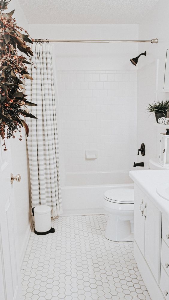 a cute little white bathroom done with square and hex tiles, a white vanity, black fixtures and some potted greenery