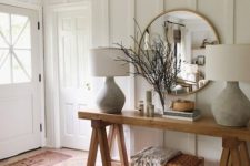 a farmhouse entryway with white paneled walls, wooden furniture, chic lamps and much natural light