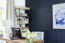 a farmhouse home office with a navy paneled wall, a bold artwork, a wooden desk and a basket plus a storage unit