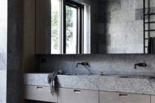 a gorgeous minimalist grey bathroom made of stone slabs, with an oversized mirror and a cool oval tub