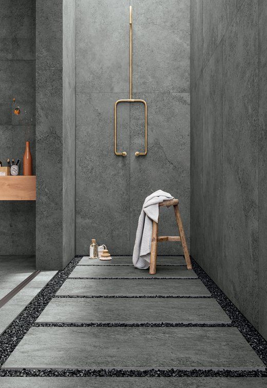 a grey concrete bathroom with pavement tiles and gravel on the floor plus gold fixtures to add chic to the space