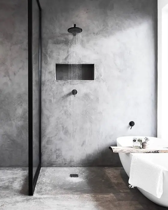 a grey minimalist bathroom done with concrete, with black fixtures and a wooden cuddy on the bathtub