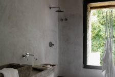 a grey wabi-sabi bathroom with concrete walls, grey tiles, stone sinks and a large window to enjoy the views