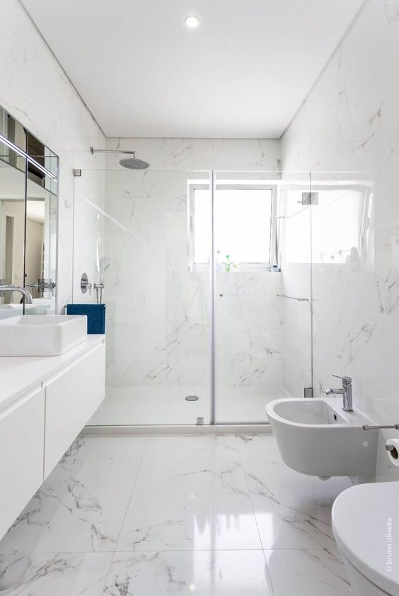 a large white bathroom with marble tiles, a floating vanity, a shower space with a window, white appliances