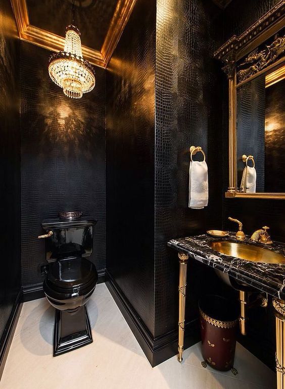 a luxurious powder room with black leather walls, a crystal chandelier, a black toilet, a black marble vanity and a gold sink