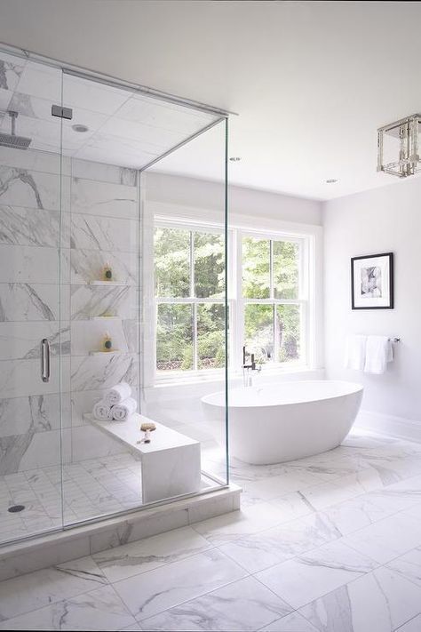 a luxurious white bathroom clad with white marble tiles and a large window for more natural light inside