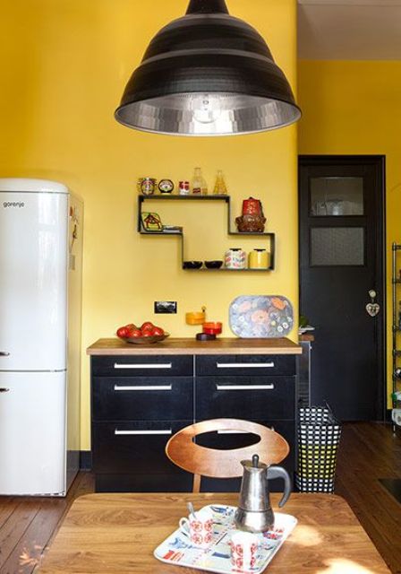 a mid-century modern kitchen with yellow walls, black cabinets, a black door and a lamp for a statement look