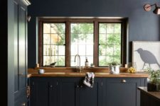 a midnight blue kitchen – cabinetry and walls, with rich stained wooden countertops and copper lamps