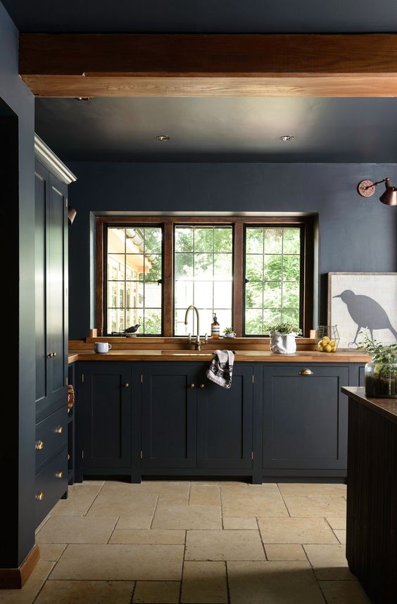 A midnight blue kitchen   cabinetry and walls, with rich stained wooden countertops and copper lamps