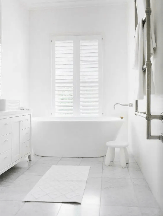 a minimalist all-white space with a stool, a large vanity and a free-standing bathtub