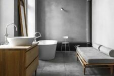 a minimalist bathroom with concrete walls, concrete tiles on the floor, a sleek vanity and a daybed, a chic bathtub