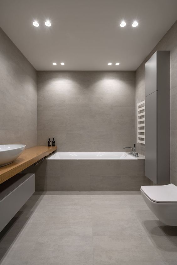 a minimalist grey and taupe bathroom clad with large scale tiles, with a sleek storage unit and a wooden vanity
