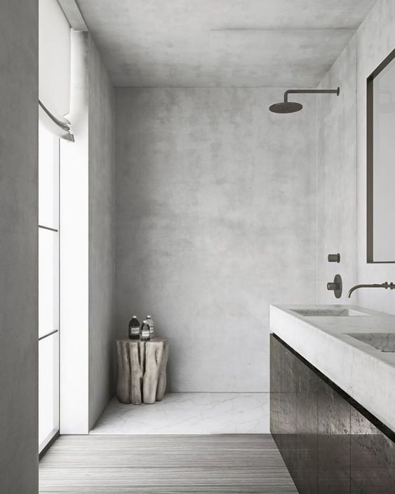 a minimalist grey bathroom clad with concrete and with greyish wood on the floor, with a large window and a black vanity
