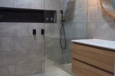 a minimalist grey bathroom clad with tiles, with a floatign vanity and a pendant lamp plus black fixtures