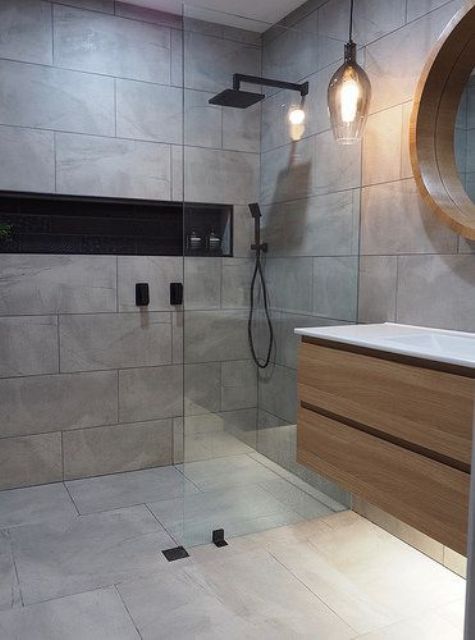 a minimalist grey bathroom clad with tiles, with a floatign vanity and a pendant lamp plus black fixtures