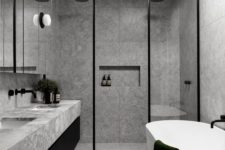 a minimalist grey bathroom done with grey marble tiles, glass doors, touches of black for drama and a skylight
