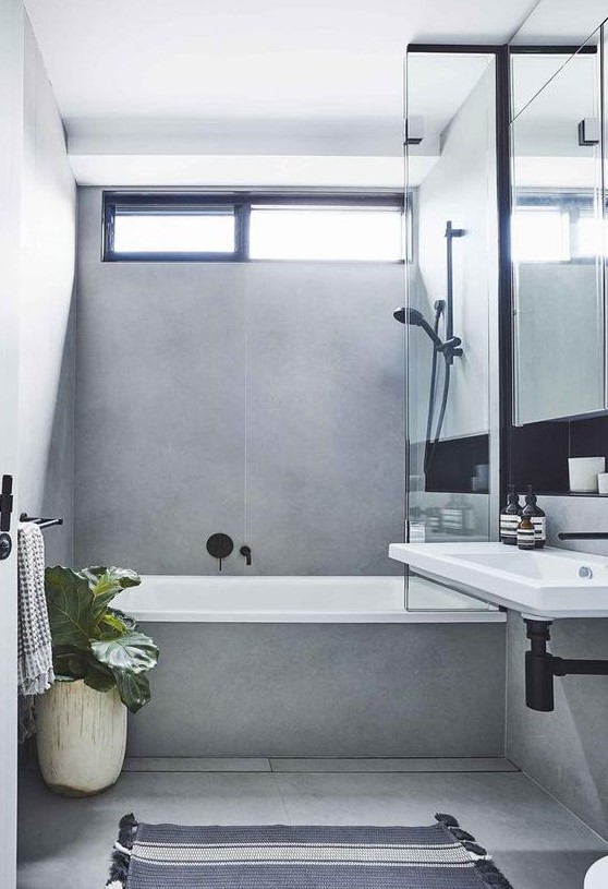 A minimalist grey bathroom done with large scale tiles, with black fixtures and potted plants plus a wall mounted sink