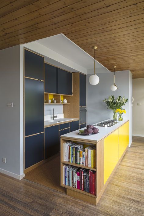 a minimalist kitchen done in navy and bright yellow, with natural wood touches and pendant lamps