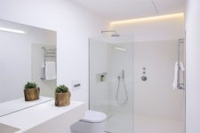 a minimalist white bathroom with a skylight, a floating vanity, a seamless glass shower space and built-in lights