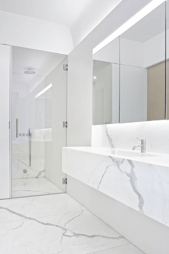 a minimalist white marble bathroom with a shower space, a floating vanity, a statement mirror and built-in lights