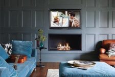 a modern luxurious living room with grey paneled walls, blue furniture and a built-in fireplace and TV