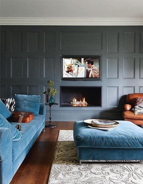 A modern luxurious living room with grey paneled walls, blue furniture and a built in fireplace and TV