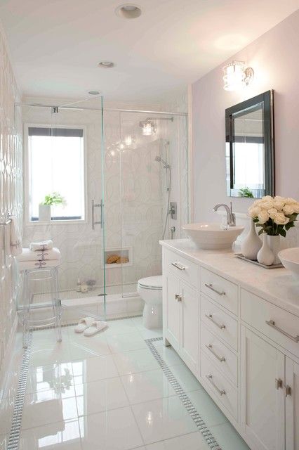 a modern white bathroom with a shower space, a vanity, a mirror with lamps, a window and some blooms