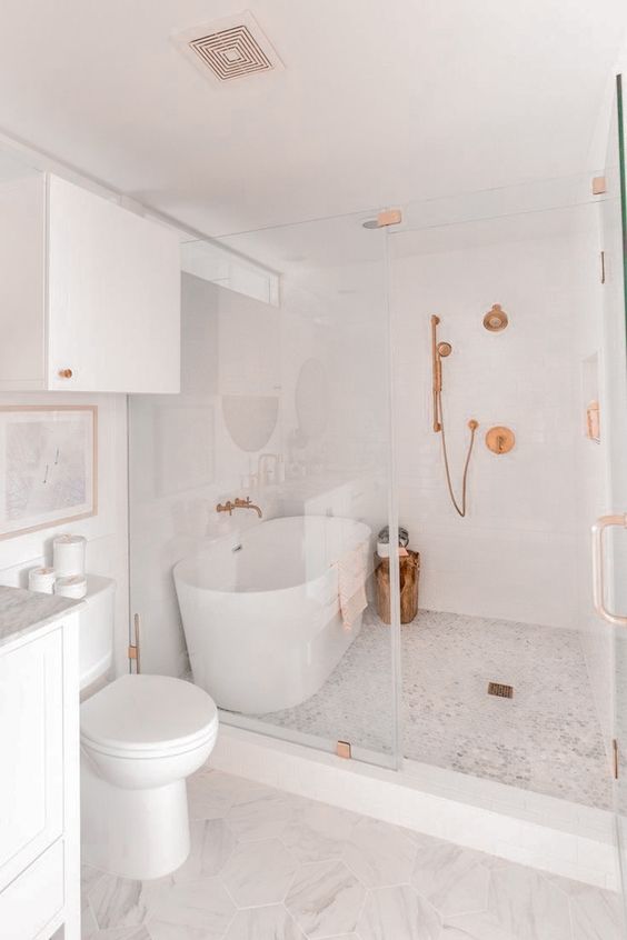 a modern white bathroom with a shower space and a tub, white appliances and a vanity and copper fixtures