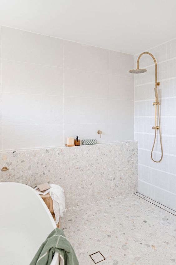 a modern white bathroom with square tiles and terrazzo, a shower space and a tub and gold fixtures