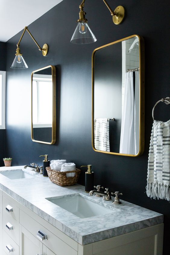 a moody bathroom with midnight blue walls, gold frame mirrors, gold sconces and other touches for more chic