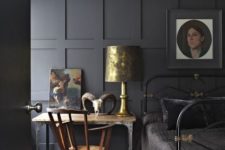 a moody bedroom with an elegant charcoal grey paneled wall, a black metal bed and vintage decor and artworks