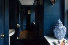 a moody navy powder room with all-navy walls, chic gold fixtures and lamps and white stone touches here and there