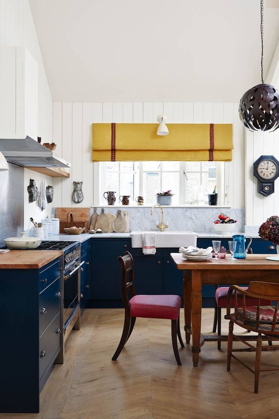 a navy and white kitchen with white stone countertops, a yellow curtain and brigth red chairs looks cool and eclectic