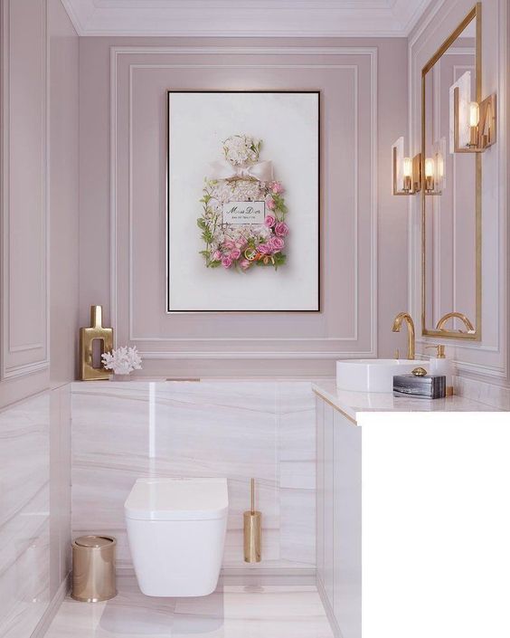 a pale pink powder room with white and pink marble tiles, gold accessories and framing for a chic and glam touch