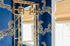 a quirky powder room with blue zebra print wallpaper, a catchy and bold chandelier, a gold frame mirror is wow