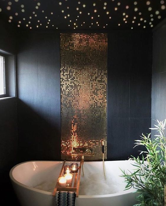 a refined bathroom with matte navy tiles, a gold tile backsplash, built-in lights and candles is a dreamy space to be