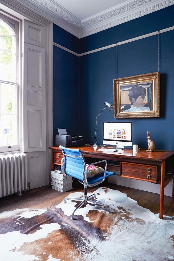 a refined blue home office with panels, a beautiful ceiling, a chic stained wooden desk, a catchy artwork