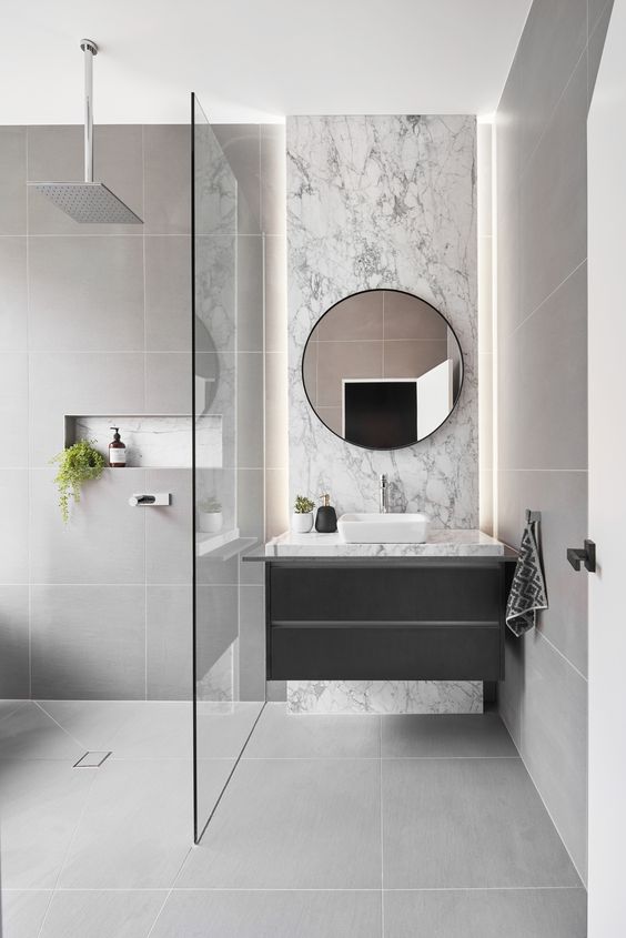 a refined grey bathroom clad with large scale tiles, with white marble and a floating vanity plus greenery