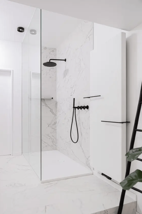 a refined minimalist bathroom done with white marble, a shower space, black fixtures and lots of light