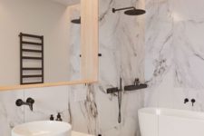 a refined white bathroom done with large scale marble tiles, with black fixtures and a large mirror in a wooden frame